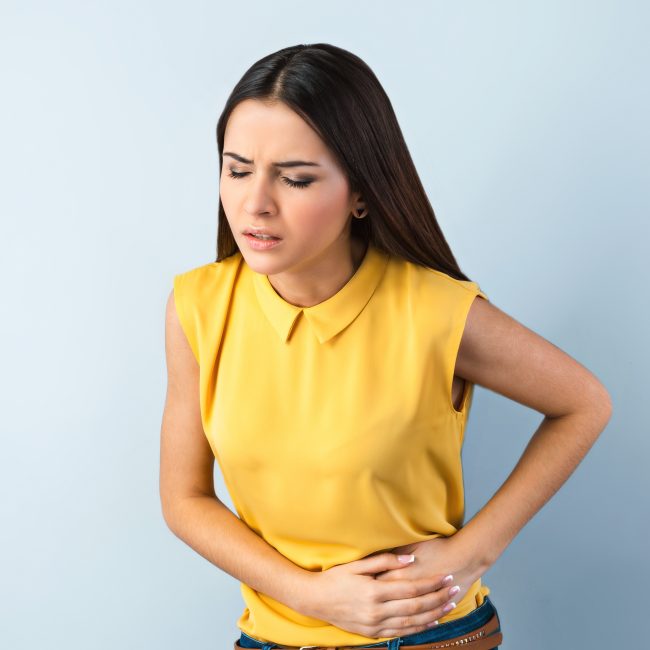 Girl-holding-her-stomach-in-pain-wearing-yellow-top-and-jeans