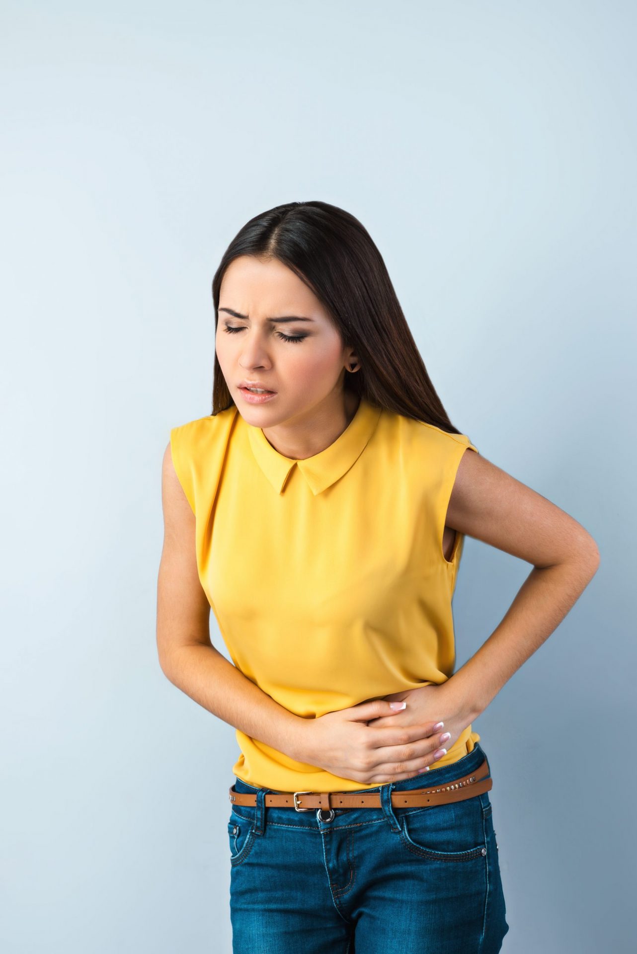 Girl-holding-her-stomach-in-pain-wearing-yellow-top-and-jeans