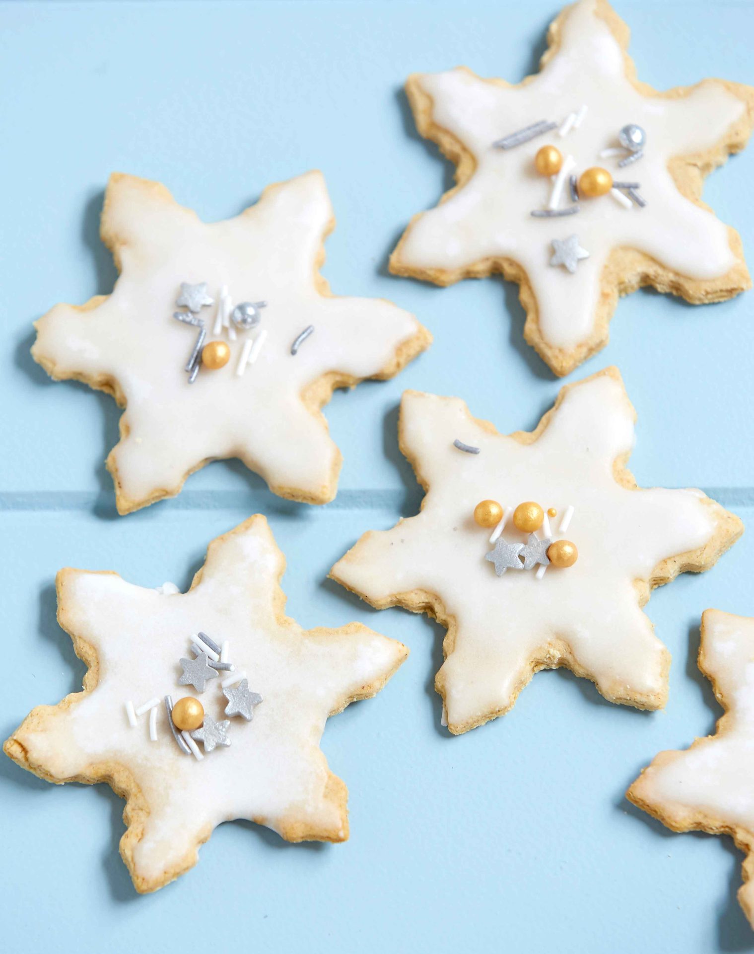 low FODMAP gingerbread snowflake cookies with white roayl icing and silver and gold sprinkles arranged on a pale blue wooden board.