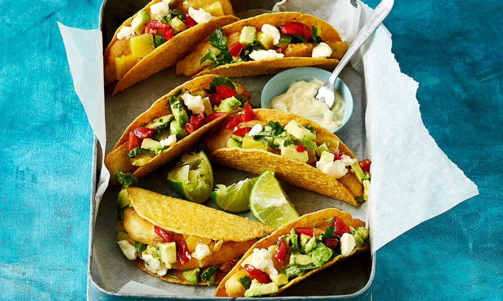 A large roasting pan is linked with baking paper. Inside crispy low FODMAP fish tacos are arranged ready to be served.