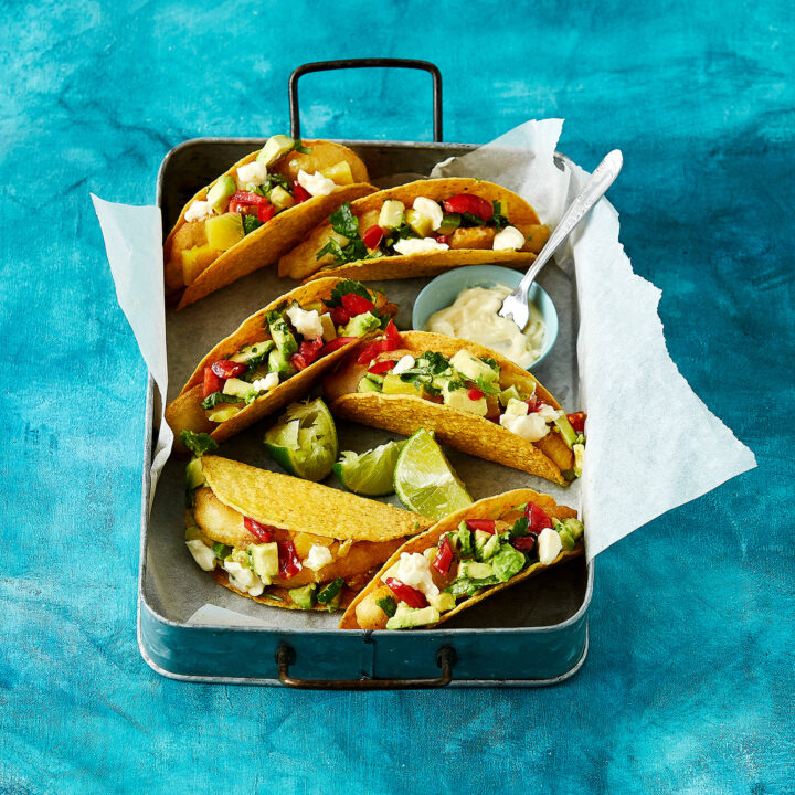 A large roasting pan is linked with baking paper. Inside crispy low FODMAP fish tacos are arranged ready to be served.