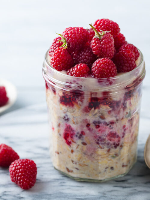 low FODMAP bircher muesli served in a glass jar and topped with a low FODMAP serve of fresh raspberries. A gold spoon sits to the side ready to enjoy.