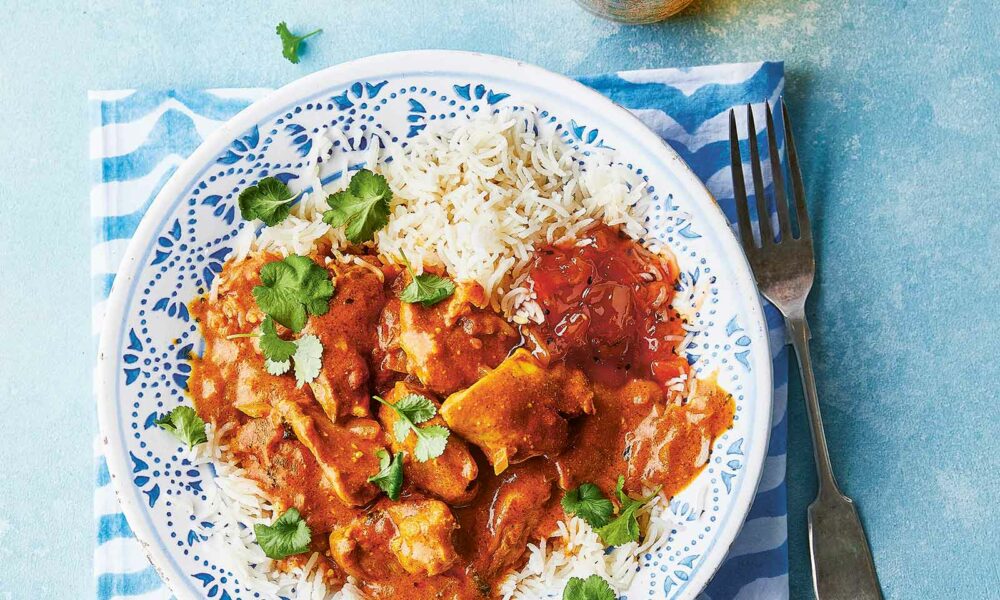 Plate of slow cooker butter chicken served with rice and a side of chutney, garnished with fresh coriander.