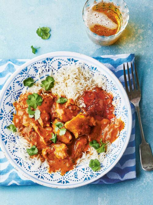 Plate of slow cooker butter chicken served with rice and a side of chutney, garnished with fresh coriander.