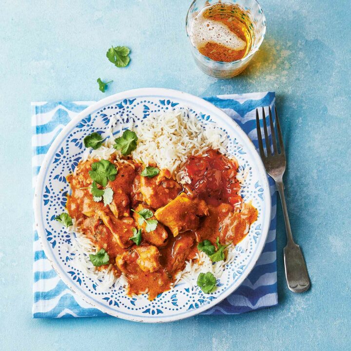 Plate of slow cooker butter chicken served with rice and a side of chutney, garnished with fresh coriander.