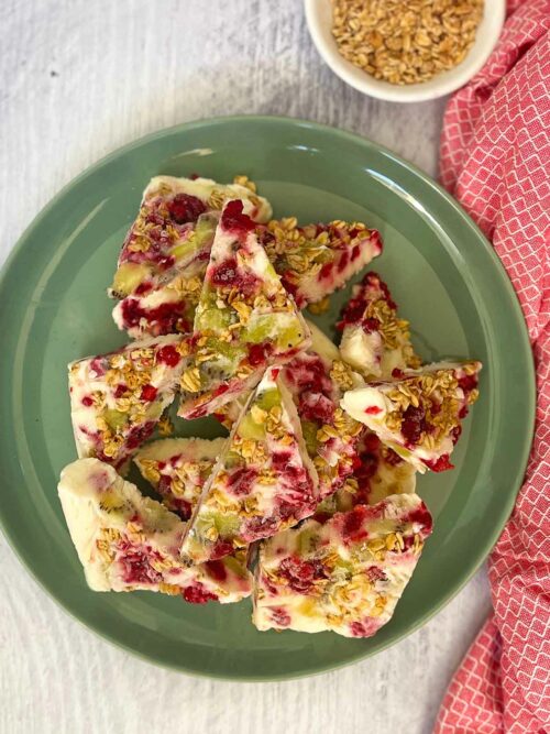 Low FODMAP Kiwi Frozen Yoghurt park with frozen raspberries and low fodmpa granola has been broken into pieces and arranged on a green plate to serve.