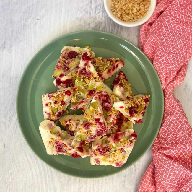 Low FODMAP Kiwi Frozen Yoghurt park with frozen raspberries and low fodmpa granola has been broken into pieces and arranged on a green plate to serve.